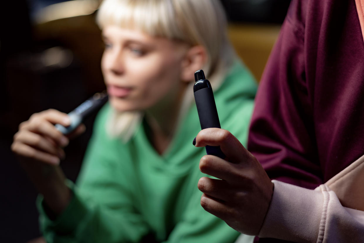 Close up of unrecognizable woman smoking electronic cigarette with her friend.