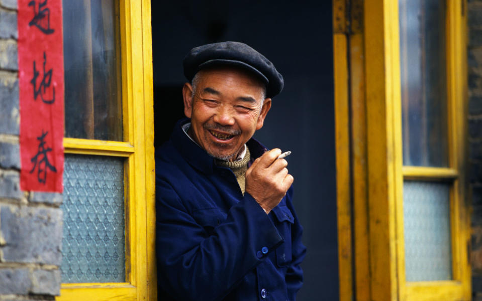 Smiling and smoking, a man leans on a doorway in Guizhou - Credit: GETTY