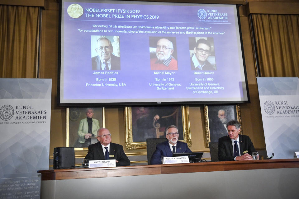 Goran K Hansson, centre, Secretary General of the Royal Swedish Academy of Sciences, and academy members Mats Larsson, left, and Ulf Danielsson, announce the winners of the 2019 Nobel Prize in Physics, during news conference at the Royal Swedish Academy of Sciences in Stockholm, Sweden, on Tuesday Oct. 8, 2019. The 2019 Nobel Prize in Physics is awarded to, seen from left on the screen, James Peebles, Michel Mayor and Didier Queloz. (Claudio Bresciani / TT via AP)