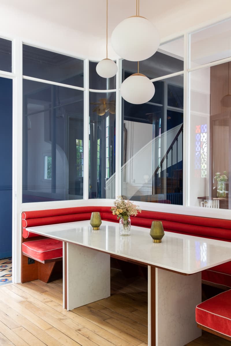 Red banquette in newly renovated dining room with pendant lamps hung above table.