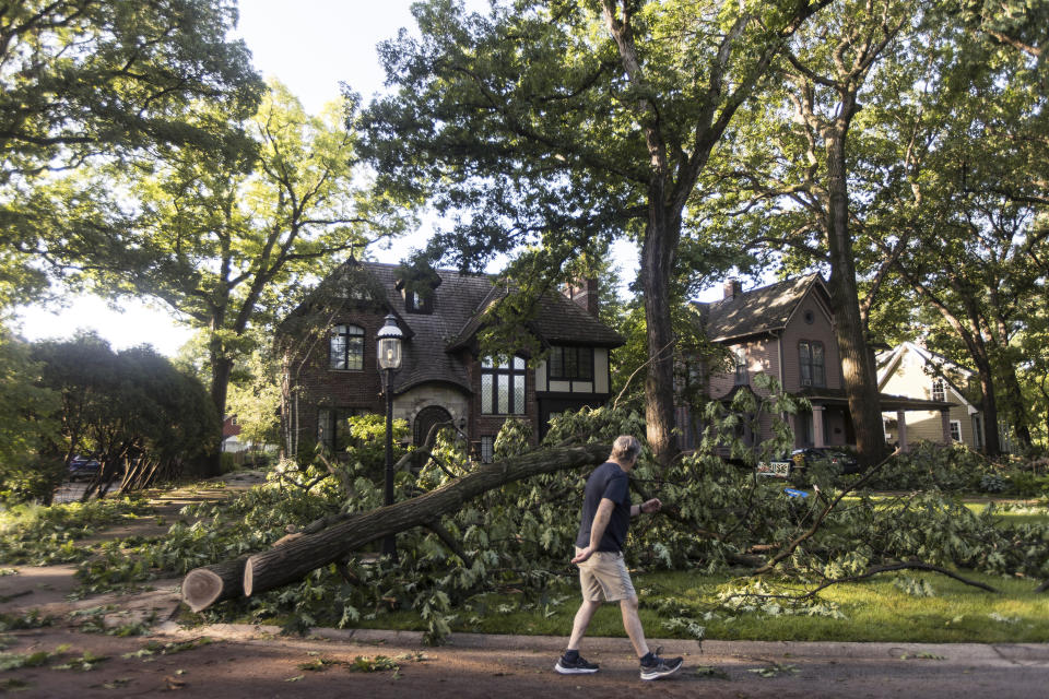 A person walks past a home in Riverside where residents begin cleanup from Monday evening's storm that raced across the Chicago area on Tuesday, June 14, 2022. A supercell thunderstorm with winds in excess of 80 mph (129 kph) toppled trees and damaged power lines Monday evening as it left a trail of damage across the Chicago area and into northwestern Indiana, the National Weather Service said. (Steven Rosenberg/Chicago Tribune via AP)