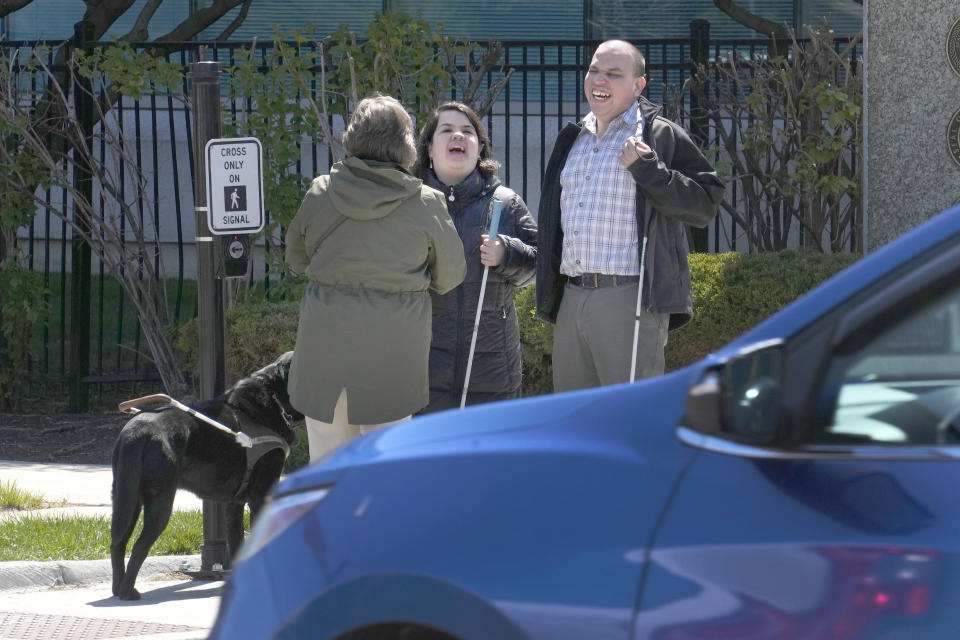 Maureen Reid, left, and her guide dog, Gaston, laughs with Sandy Murillo, center, and Geovanni Bahena, before they navigate Rosevelt Avenue, with audible signals for the blind, on Wednesday, April 26, 2023, in Chicago. A federal court ruling slamming street crossing signals in Chicago as dangerous for blind and low-vision residents are giving momentum to advocates who say the community has long been left out of the push for safer streets. (AP Photo/Charles Rex Arbogast)