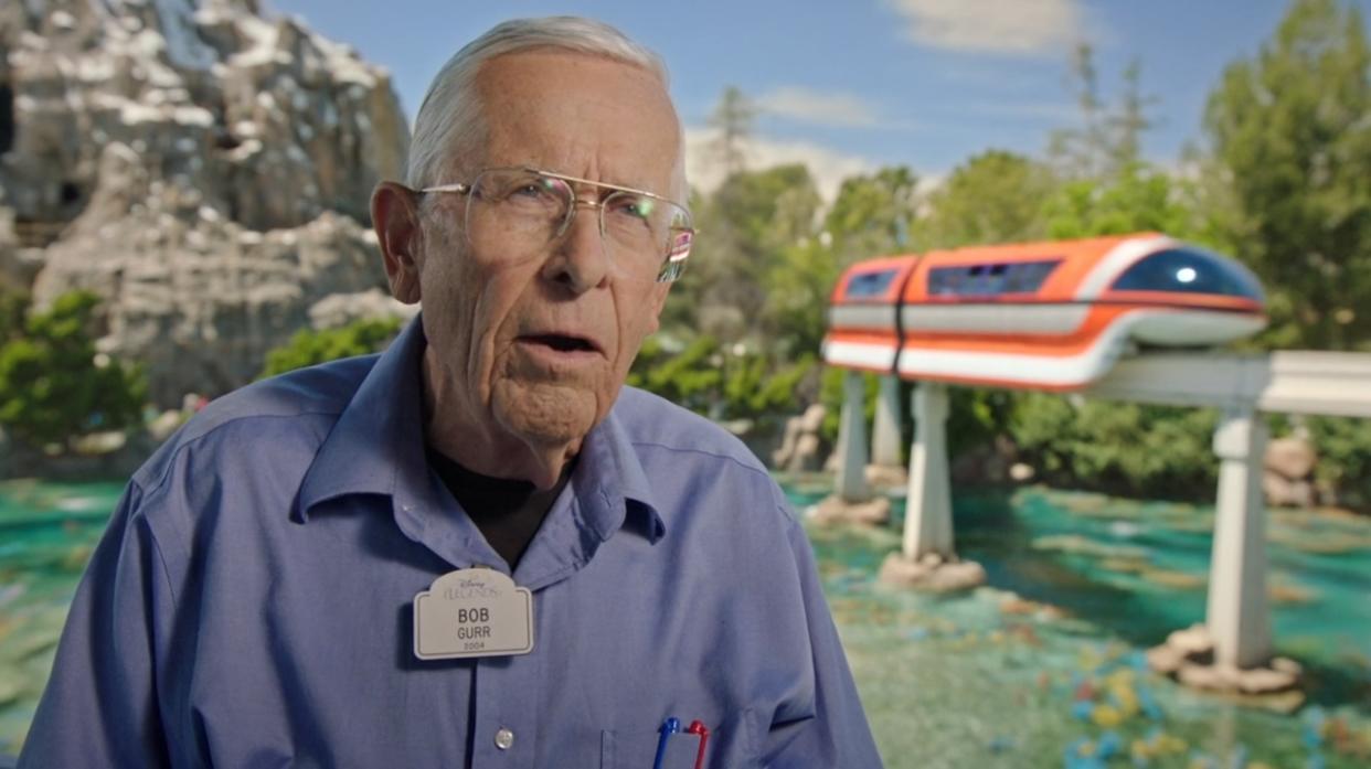  Bob Gurr talking in front of Matterhorn and Monorail in The Imagineering Story. 