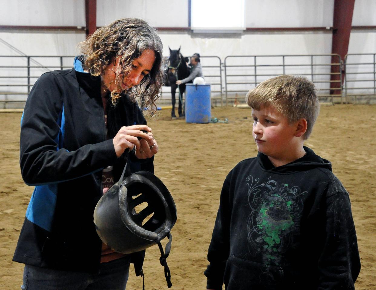 Stirrup Courage founder Tara Steiner adjusts a safety helmet for Landon Vierheller before he rides a horse.