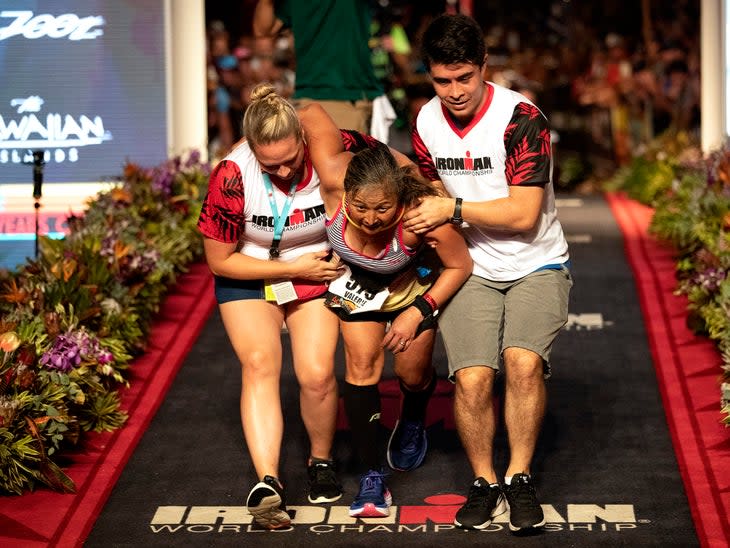 An athlete is helped across the finish line at Ironman Kona Alii Drive