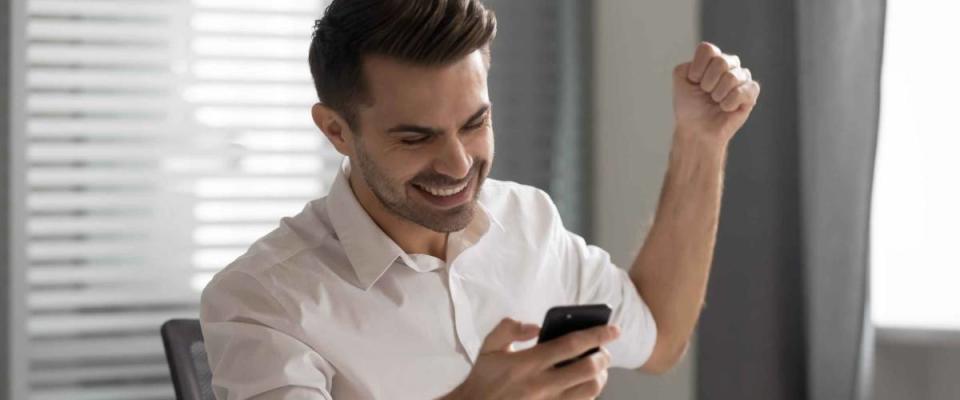 Overjoyed excited young businessman sees on his smartphone that his stocks are performing well