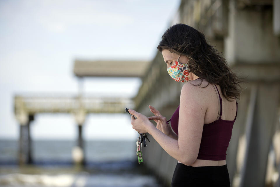 A Tybee Island, Ga., resident uses her phone to text a friend near the pier on the south side of Tybee beach while wearing a handmade mask Saturday, April 4, 2020. On Friday, Gov. Bryan Kemp opened the state's outdoor space by signing an executive order that allows people to exercise outside, with social distancing of at least six feet because of the coronavirus outbreak. (Stephen B. Morton/Atlanta Journal-Constitution via AP)