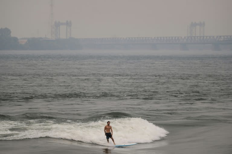 Ein Mann surft im Sankt-Lorenz-Strom mit Rauch, der durch Waldbrände im Norden Quebecs im Hintergrund verursacht wurde, in Montreal, Kanada, am 25. Juni 2023 (ANDREJ IVANOV)