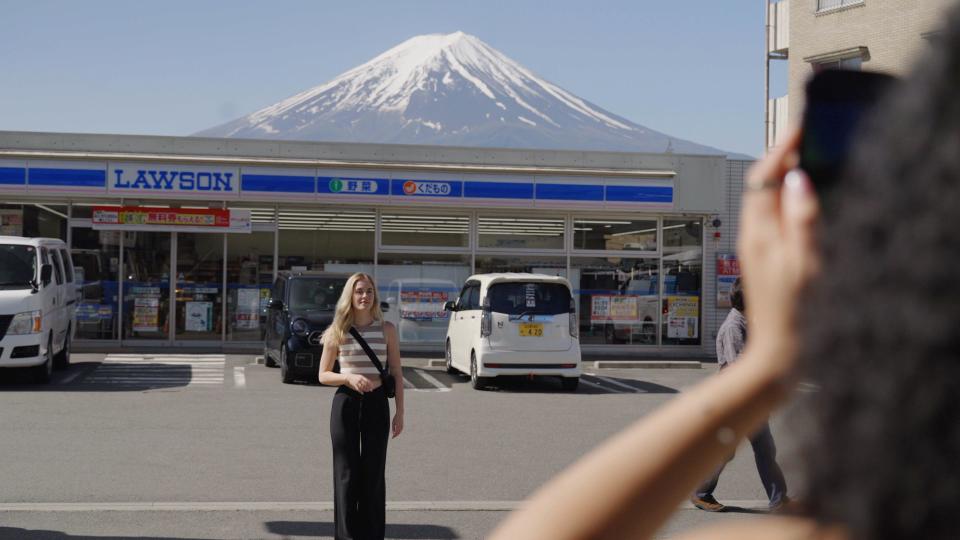 Woman takes photo of another woman standing across the street in front of supermarket