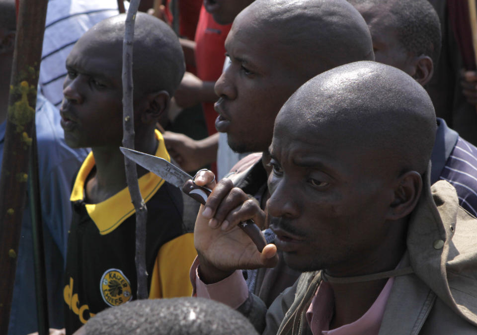 A striking mine worker armed with a knife joins others armed with machetes, sticks, and spears in a march to a smelter plant at the Lonmin Platinum Mine near Rustenburg, Wednesday, Sept, 12, 2012 to hand over a memorandum to mine management and to ensure that workers had not reported for duty. Miners are refusing to return to work until their demands over low pay and working conditions are met. Strikes are spreading to nearby gold mines. (AP Photo/Denis Farrell)