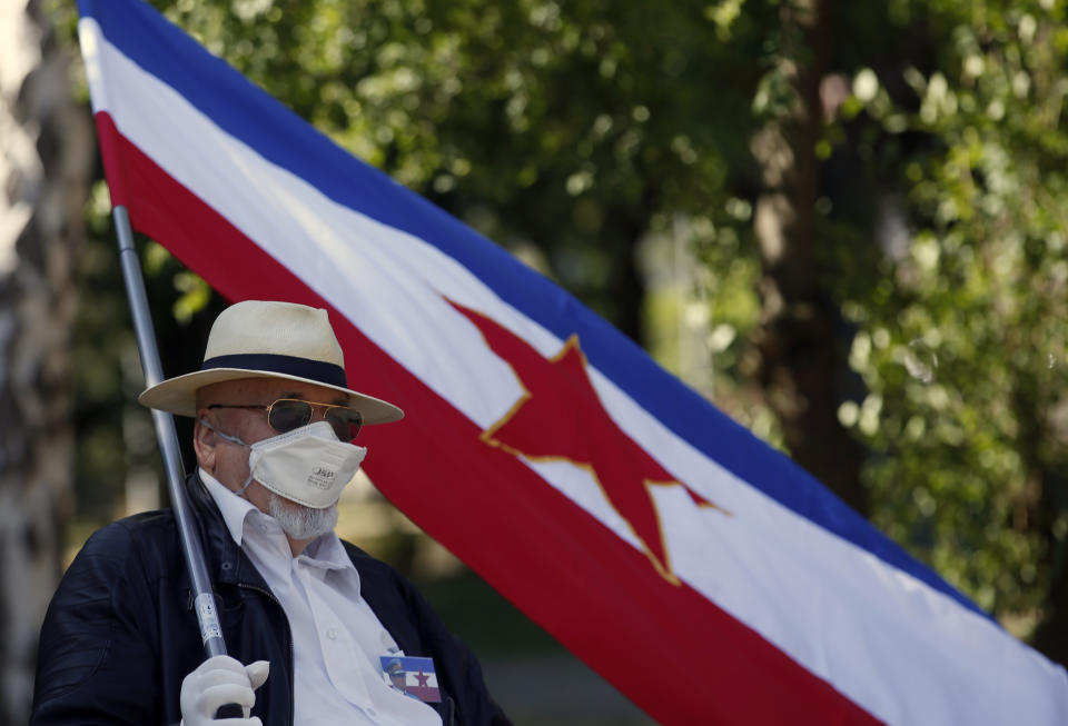 A supporter of the late Yugoslav communist president Josip Broz Tito wearing a mask to protect against coronavirus holds an old Yugoslav flag with the communist five-point star in front of memorial complex prior to a wreath laying ceremony in Belgrade, Serbia, Monday, May 25, 2020. People flocked to Tito's grave to mark the 128th anniversary of his birth. (AP Photo/Darko Vojinovic)