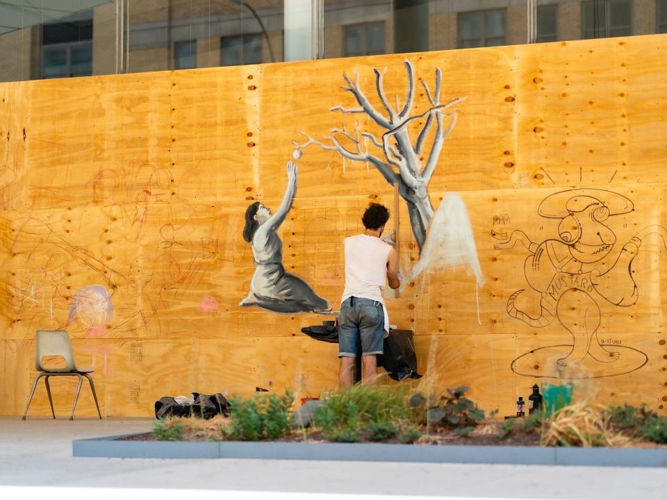 An artist paints on the boarded-up windows of the Whitney Museum of American Art in the Meatpacking District on June 21, 2020 in New York City.