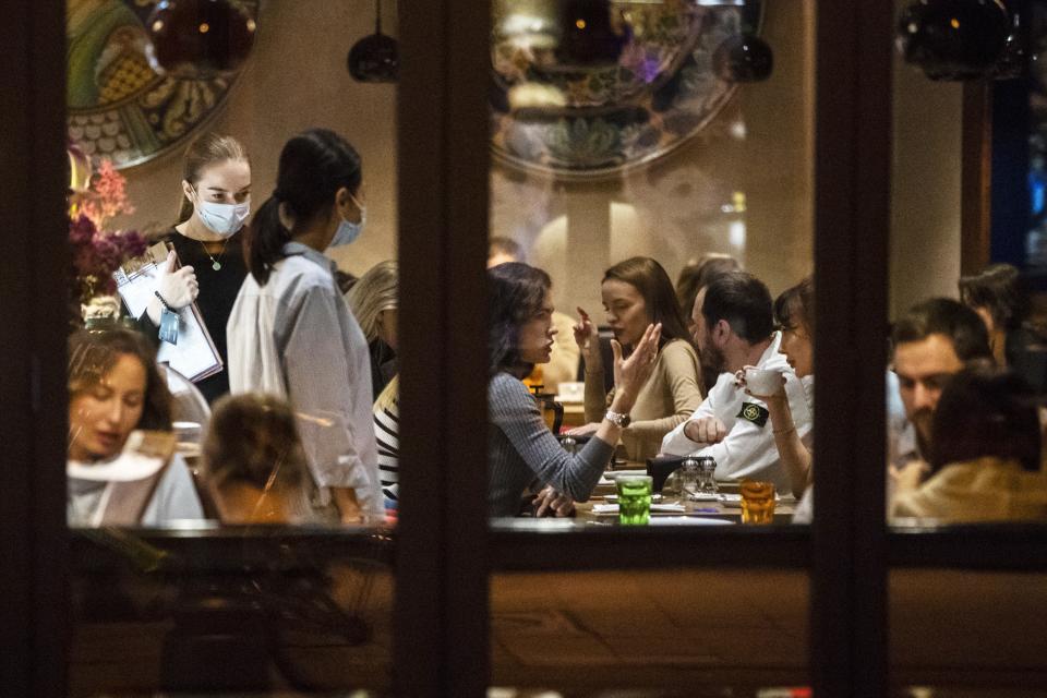 Customers sit in a restaurant at Patriarshiye Prudy, a hip restaurant and bar district in Moscow, Russia, late Friday, Oct. 16, 2020. The outbreak in Russia this month is breaking the records set in the spring, when a lockdown to slow the spread was put in place. But, as governments across Europe move to reimpose restrictions to counter rising cases, authorities in Russia are resisting shutting down businesses again. (AP Photo/Pavel Golovkin)