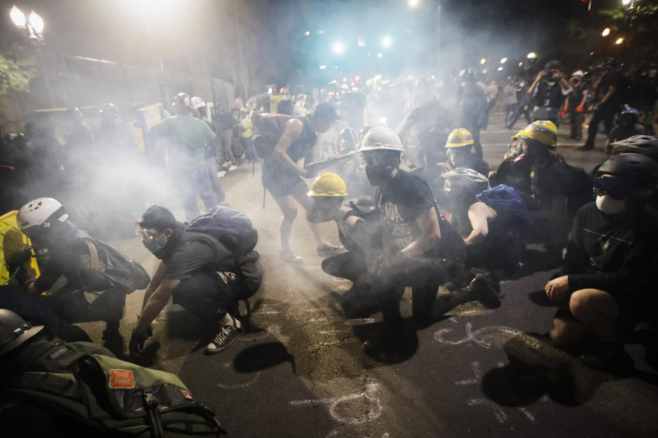 Demonstrators sit and kneel as tear gas fills the air during a Black Lives Matter protest at the Mark O. Hatfield United States Courthouse Sunday, July 26, 2020, in Portland, Ore. (AP Photo/Marcio Jose Sanchez)