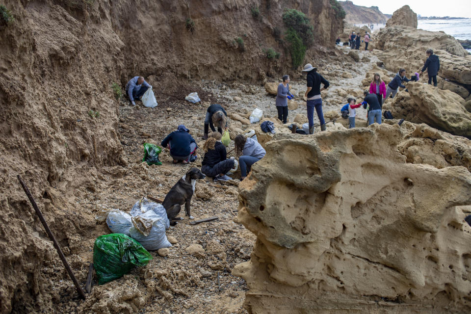 People clean tar from an oil spill in the Mediterranean sea in Gador nature reserve near Hadera, Israel, Saturday, Feb. 20, 2021. Hundreds of volunteers are taking part in a cleanup operation of Israeli shoreline as investigations are underway to determine the cause of an oil spill that threatens the beach and wildlife, at Gador Nature Reserve near the northern city of Hadera, the tar smeared fish, turtles, and other sea creatures. (AP Photo/Ariel Schalit)