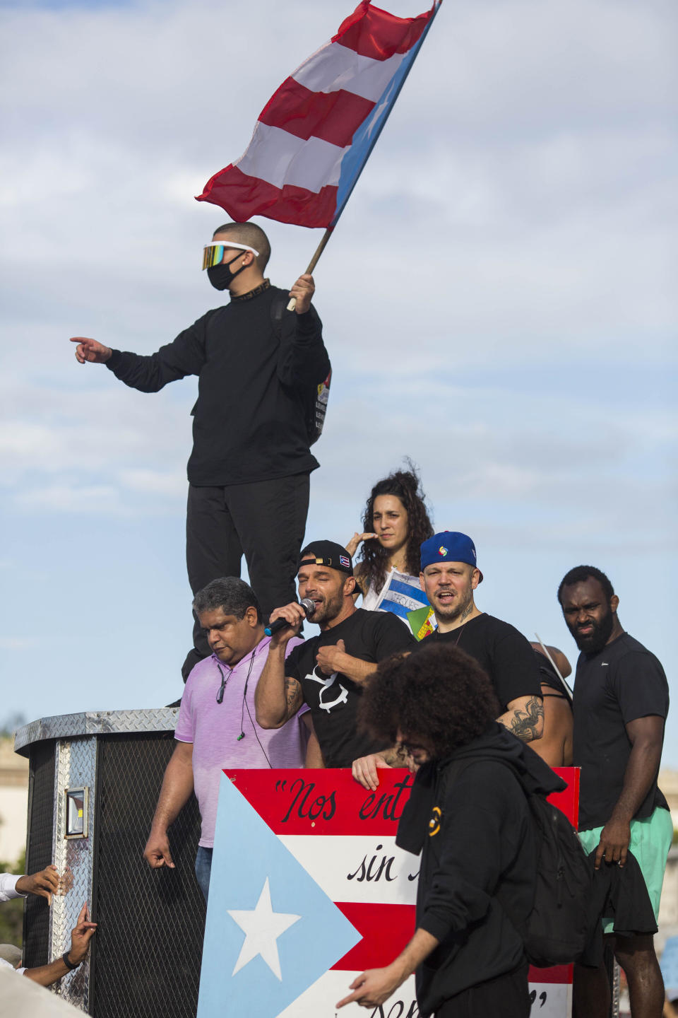 Singer Ricky Martin speaks to the crowd, accompanied by Puerto Rican rapper Rene Juan Perez known by his stage name of Residente and Benito Antonio Martinez Ocasio, known by his stage name Bad Bunny (with flag) in front of the Puerto Rican Capitol, before a protest march against governor Ricardo Rosello, in San Juan, Puerto Rico, Wednesday, July 17, 2019. Protesters are demanding Rossello step down for his involvement in a private chat in which he used profanities to describe an ex-New York City councilwoman and a federal control board overseeing the island's finance. (AP Photo/Dennis M. Rivera Pichardo)