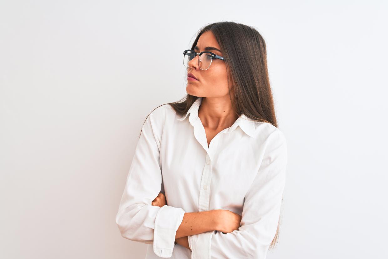 Young beautiful businesswoman wearing glasses standing over isolated white background looking to the side with arms crossed convinced and confident