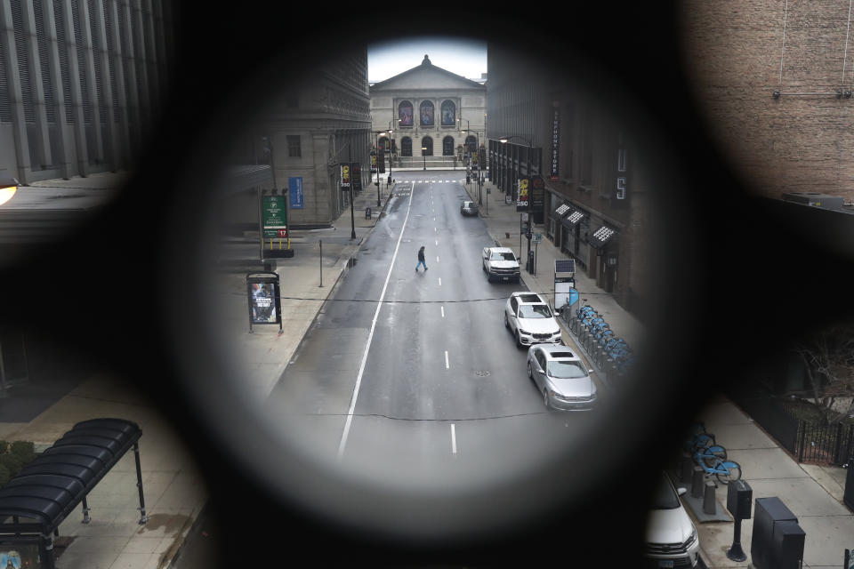 A man walks across a nearly empty Adams Street near The Art Institute of Chicago, Monday, March 23, 2020, in Chicago, on the first work day since Illinois Gov. J.B. Pritzker gave a shelter in place order last week. (AP Photo/Charles Rex Arbogast)