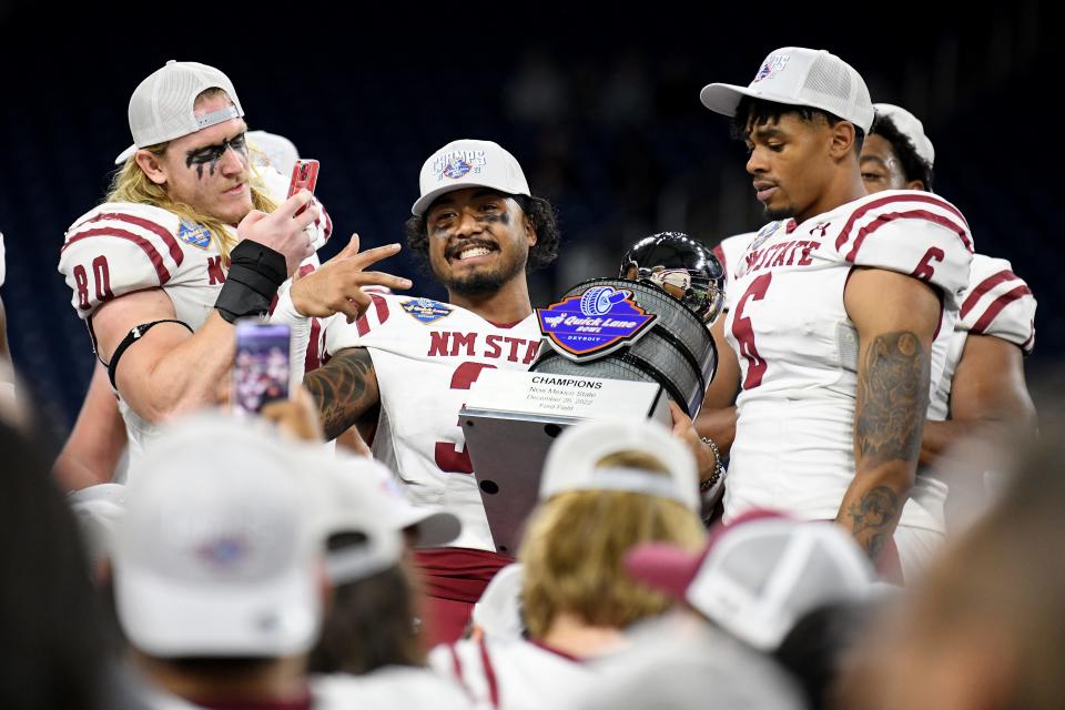 Dec 26, 2022; Detroit, Michigan, USA; New Mexico State University linebacker Trevor Brohard (left) takes a picture of safety Bryce Jackson (center) holding the Quick Lane Bowl trophy on the podium during their post-game celebration after their win over Bowling Green State University in the 2022 Quick Lane Bowl at Ford Field. Mandatory Credit: Lon Horwedel-USA TODAY Sports