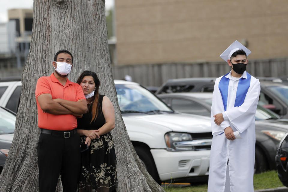 A graduate stands near family members as the New Orleans Charter Science and Math High School class of 2020 holds a drive-in graduation ceremony as a result of the COVID-19 pandemic, outside Delgado Community College in New Orleans, Wednesday, May 27, 2020. Students and family got out of their cars to receive diplomas one by one, and then held a parade of cars through city streets. (AP Photo/Gerald Herbert)