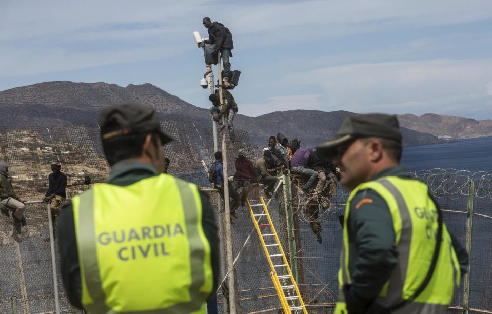 Spanish Guardia Civil officers stand guard as sub-Saharan migrants sit on top of a metallic fence that divides Morocco and the Spanish enclave of Melilla, Thursday, April 3, 2014. Spanish and Moroccan police have thwarted a fresh attempt by dozens of African migrants to try to scale border fences to enter the Spanish enclave of Melilla. Thousands of sub-Saharan migrants seeking a better life in Europe are living illegally in Morocco and regularly try to enter Melilla in the hope of later making it to mainland Spain. (AP Photo/Santi Palacios)