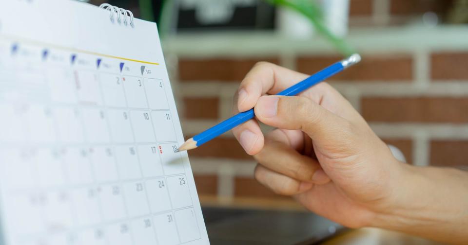 Person marking a date on a paper monthly calendar with a blue pencil