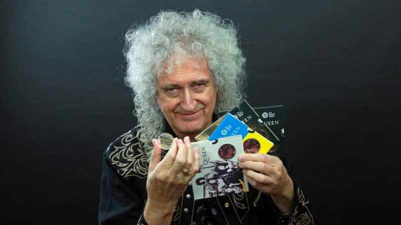 Foto del guitarrista de Queen, Brian May, sosteniendo una moneda conmemorativa de la banda británica