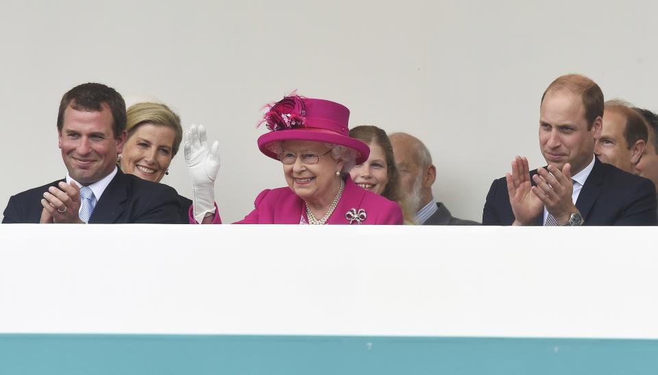 Peter Phillips (L) and Prince William, Duke of Cambridge (R) look on as Queen Elizabeth II waves to guests attending 