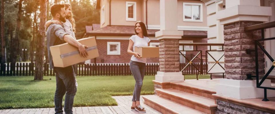 Happy couple is standing near new house with cardboard boxes. Moving day.