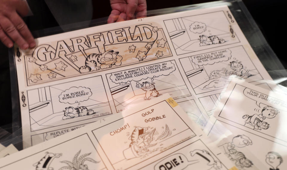 In this Monday, Nov. 18, 2019 photo, Heritage Auctions collectibles specialist Brian Wiedman displays Garfield comic artwork drawn by creator Jim Davis in Dallas. Thousands of the comics drawn by Davis are going up for auction. (AP Photo/LM Otero)