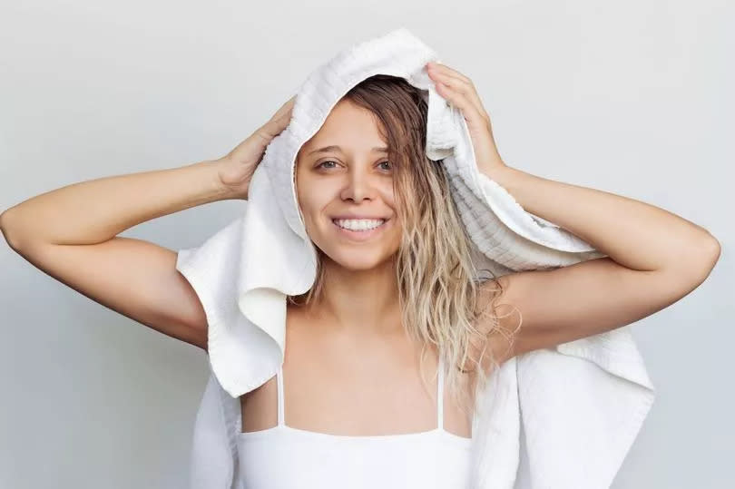 A young charming caucasian smiling blonde woman dry her wet hair with a white towel on her head after a shower isolated on a gray background.