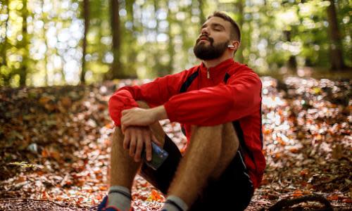 Portrait of relaxed young man with bluetooth headphones in forest