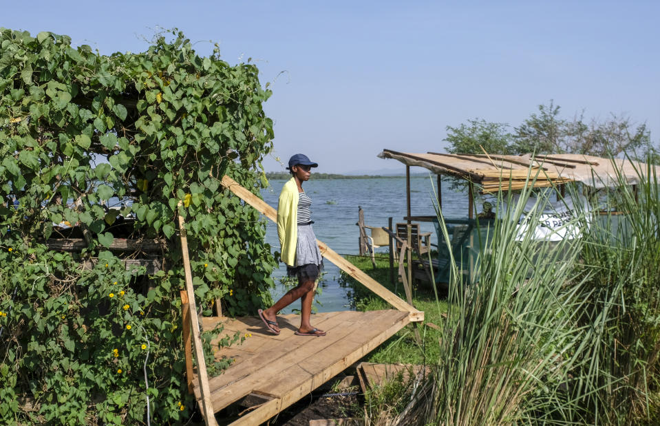 A woman stands at the entrance to a floating restaurant and bar, on Lake Victoria near the Luzira area of Kampala, Uganda Sunday, Feb. 19, 2023. Flowering plants rise from the water into the wooden hull of James Kateeba's boat, used as a floating restaurant and bar that can be unmoored to drift for pleasure, but the greenery emerges from an innovative recycling project which uses thousands of dirt-encrusted plastic bottles to anchor the boat. (AP Photo/Hajarah Nalwadda)