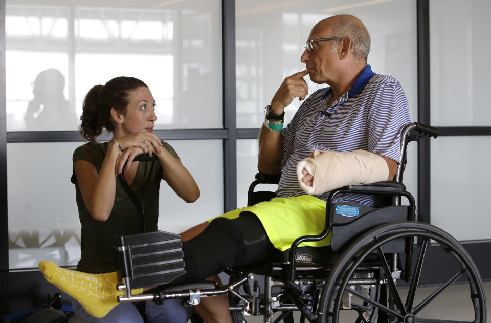 William Lytton, of Scarsdale, N.Y., right, speaks with physical therapist Caitlin Geary during physical therapy at Spaulding Rehabilitation Hospital, in Boston, Tuesday, Aug. 28, 2018, while recovering from a shark attack. Lytton suffered deep puncture wounds to his leg and torso after being attacked by a shark on Aug. 15 while swimming off a beach, in Truro, Mass. Lytton injured a tendon in his arm while fighting off the shark. (AP Photo/Steven Senne)