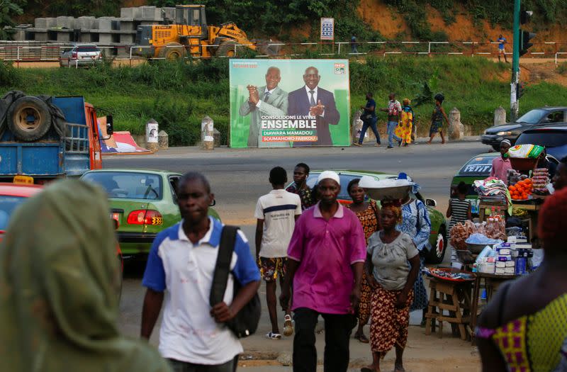 People walk pass next to a campaign billboard showing the candidats of the ruling coalition party, the Rally of Houphouetists for Democracy and Peace (RHDP) ahead of the legislative election in Abidjan