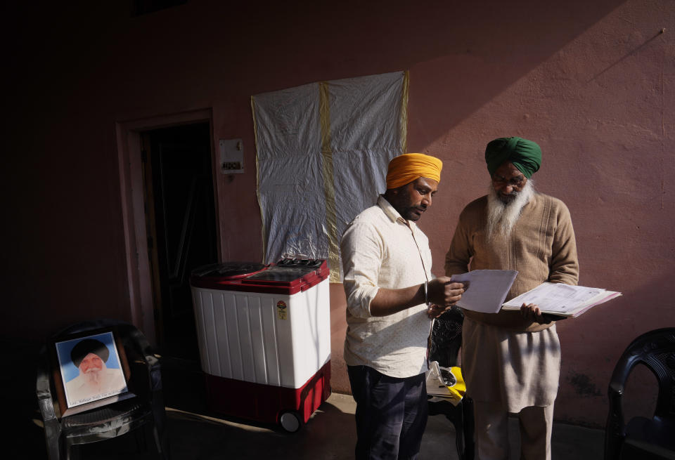 Amarjeet Singh, center, son of Sudagar Singh, seen in photograph on the left, who died during farm laws protests, shows official documents to village head Charan Singh, in his family home in Kaler Ghuman village, some 40 kilometers (24 miles) from Amritsar, in Indian state of Punjab, Tuesday, Feb. 15, 2022. India's Punjab state will cast ballots on Sunday that will reflect whether Indian Prime Minister Narendra Modi's ruling Bharatiya Janata Party has been able to neutralize the resentment of Sikh farmers by repealing the contentious farm laws that led to year-long protests. (AP Photo/Manish Swarup)