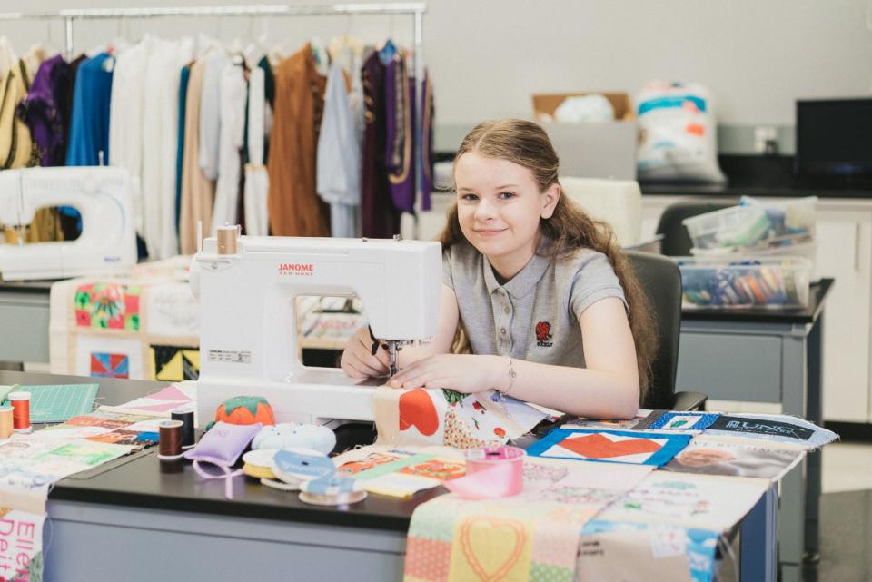 A teenager works on a quilt at a sewing machine.