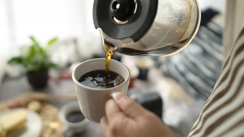 Pouring steaming coffee from a carafe into a mug