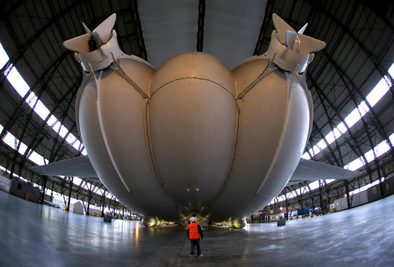 A worker stands under the Airlander 10 hybrid airship during its unveiling in Cardington