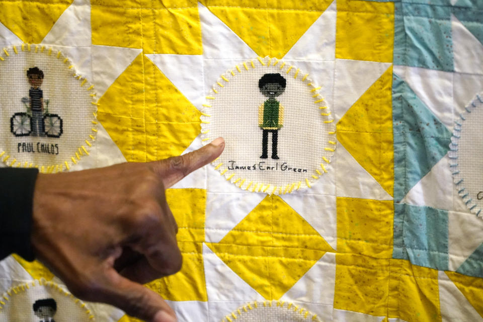 Gloria Green-McCray, sister of James Earl Green, who along with Phillip Lafayette Gibbs was killed by Mississippi Highway Patrolmen in 1970 on the campus of Jackson State University, points out the cross stitched portrait of her brother wearing his high school colors on one of the quilts on exhibit at the school, Tuesday, Nov. 30, 2021, in Jackson, Miss. Two hand crafted quilts stitched together by 75 artists from the U.S. and beyond that feature more than 115 cross-stitched portraits honoring African Americans who lost their lives to racial violence, are part of the Stitch Their Name Memorial Project, on display at the university's Margaret Walker Center. (AP Photo/Rogelio V. Solis)