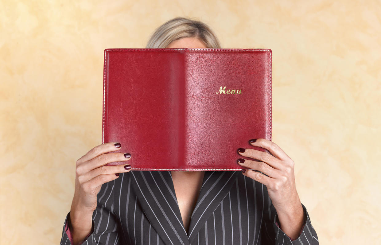 A woman holds a red menu booklet up in front of her face