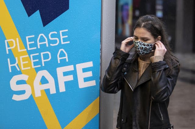 A young woman in Belfast puts on her face covering as she walks past a Covid-19 safety message from Belfast City Council 
