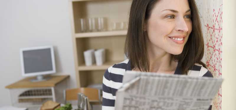 A smiling young woman looking off into the distance while holding the financial section of a newspaper.