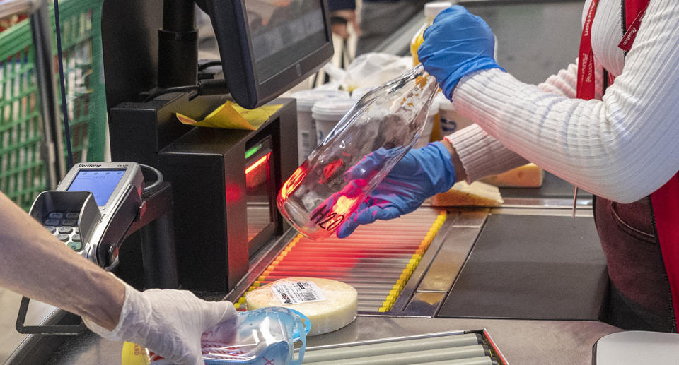 A supermarket worker wearing gloves as she scans items.