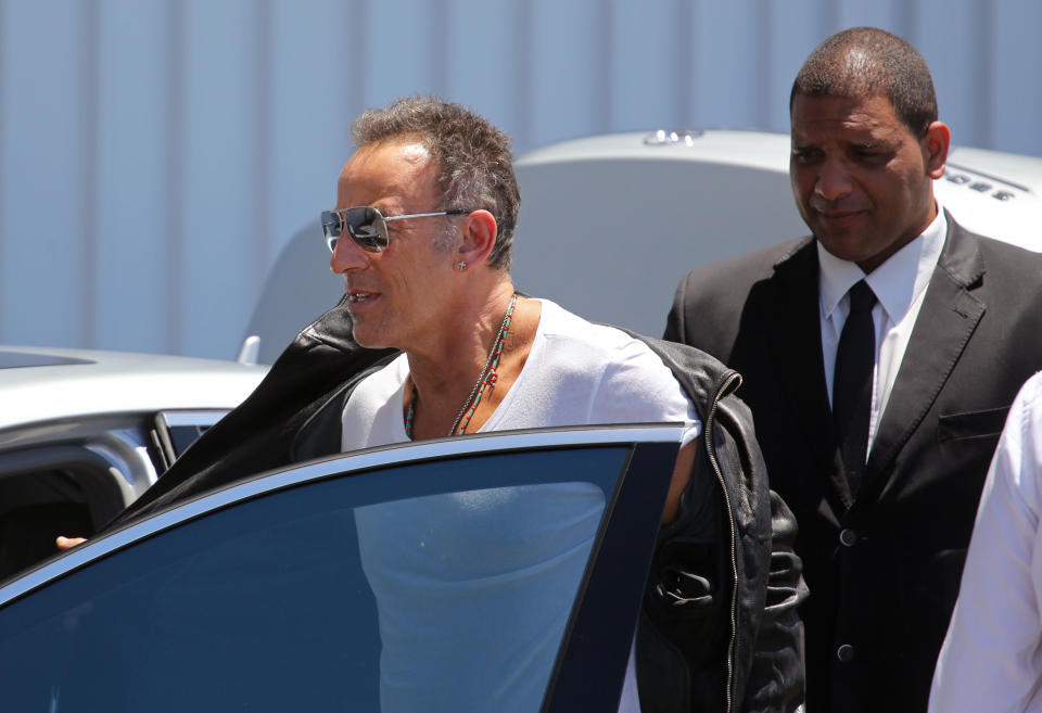 American performer Bruce Springsteen, center, removes his jacket as he arrives at the airport in Cape Town, South Africa, Friday, Jan. 24, 2014. Bruce Springsteen begin his first South African tour on Sunday, Jan. 26, in Cape Town. (AP Photo/Schalk van Zuydam)