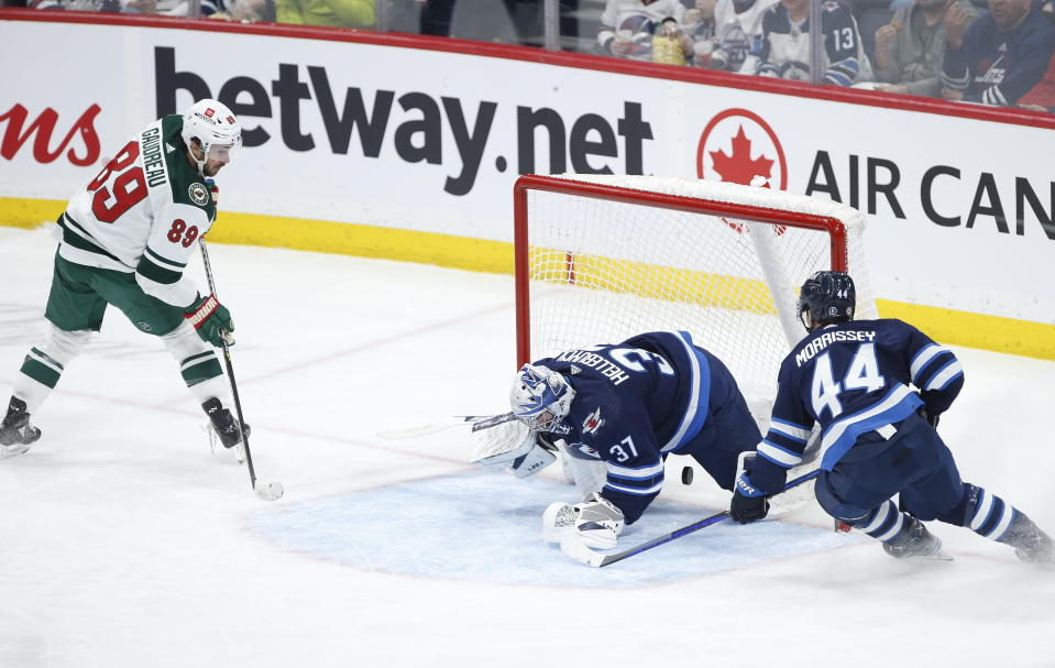 Minnesota Wild's Frederick Gaudreau (89) scores on Winnipeg Jets goaltender Connor Hellebuyck (37) as Josh Morrissey (44) defends during the second period of an NHL hockey game, Wednesday, March 8, 2023 in Winnipeg, Manitoba. (John Woods/The Canadian Press via AP)
