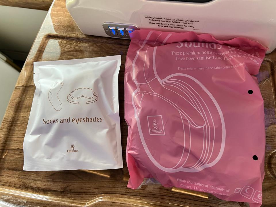 Two packages, one white one pink, containing socks, eyeshades, and headphones, displayed in Emirates business class