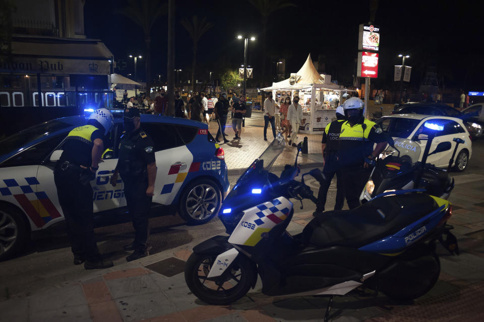 Police officers patrol as people walk on the street in Fuengirola, near Malaga, Spain, Saturday, Aug. 8, 2020. The increase in Spain of coronavirus outbreaks associated with nightlife has set off alarms in recent days, mainly in tourist areas where pubs and discos are full before the summer tourist campaign. (AP Photo/Jesus Merida)