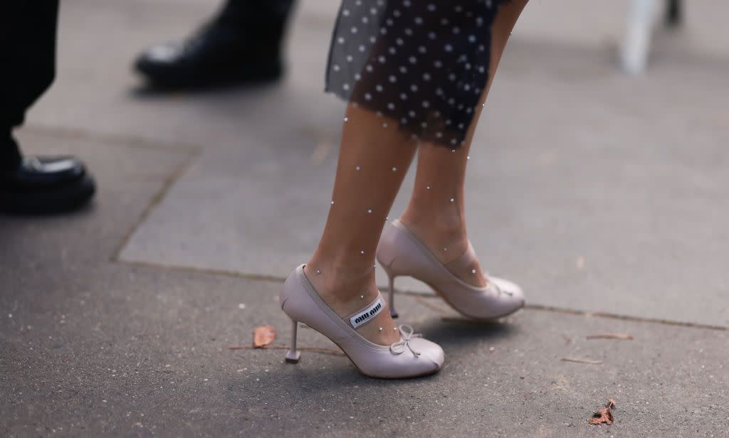 a woman wearing a pair of pink satin square toe ballet heels by miu miu with a long black and rhinestone skirt on the street in paris in a roundup of the best heels for wide feet 2024