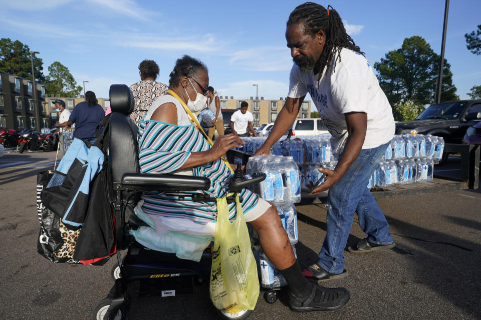 Willie Brown, right, of the AIDS Healthcare Foundation places cases of water on the chair of Diana Washington, a resident of the Golden Keys Senior Living apartments in Jackson, Miss., Thursday, Sept. 1, 2022. A recent flood worsened Jackson's longstanding water system problems. (AP Photo/Steve Helber)